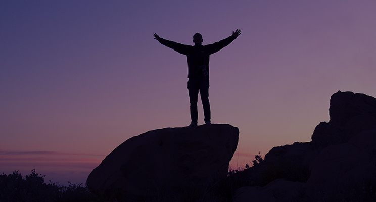 man standing on rock with arms open