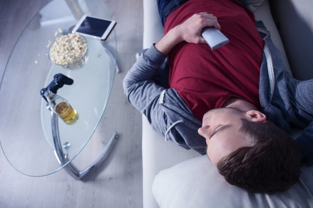 man asleep on couch with pop corn and videogame controller on table