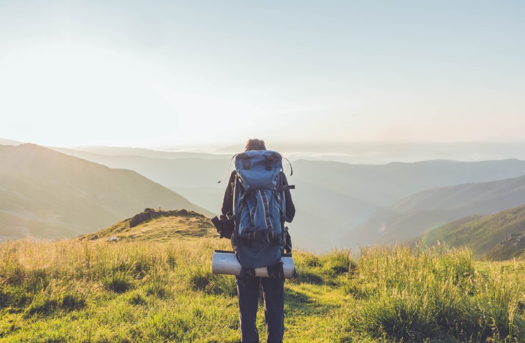 man standing at top of mountains with hiking bag